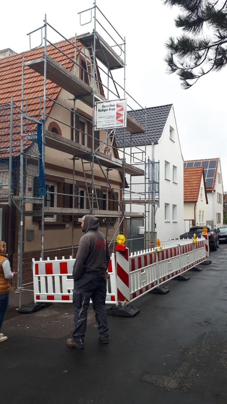 Gerüst an einem Wohnhaus in einer abgesperrten Straße mit zwei Personen im Vordergrund