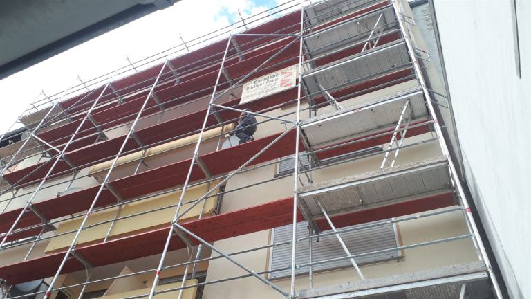 Mehrstöckiges Baugerüst an einem Wohnhaus mit einer Person auf mittlerer Ebene