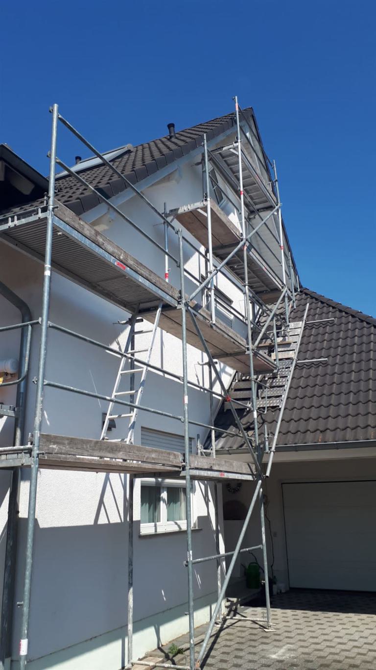 Hausfassade mit Gerüst vor dem Dachgeschoss unter blauem Himmel