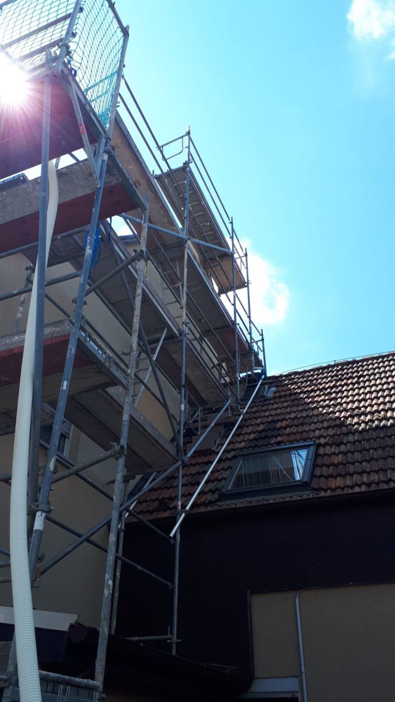 Gerüst an einem Haus mit Ziegeldach unter blauem Himmel