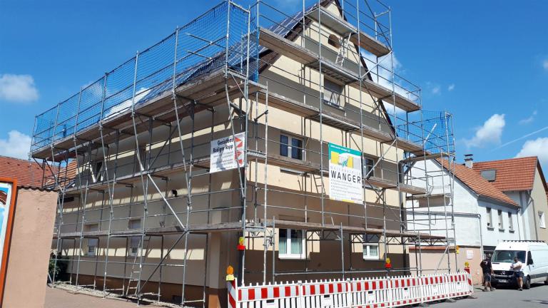Mehrstöckiges Wohnhaus mit Gerüst und Absperrung bei Bauarbeiten unter blauem Himmel