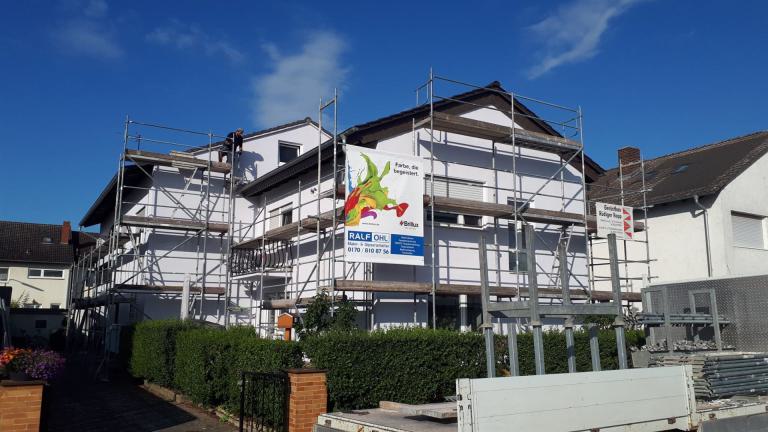 Weißes Wohnhaus mit Gerüst bei Renovierungsarbeiten unter blauem Himmel