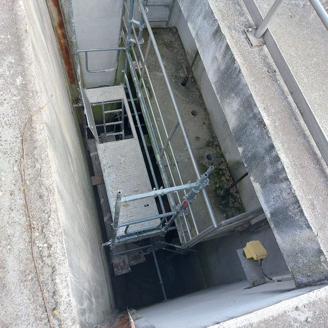 Blick von oben in einen schmalen Betonschacht mit Gerüst und Geländern